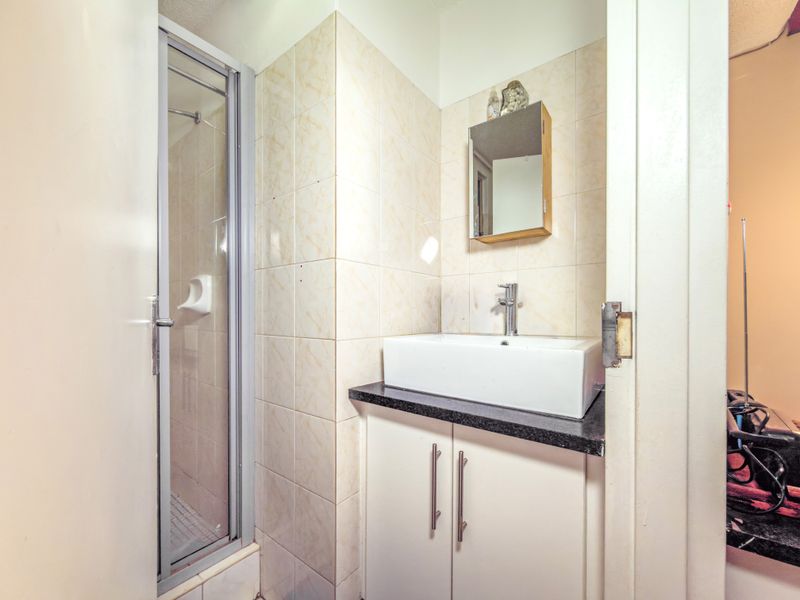 Compact bathroom featuring a shower enclosure, vanity cabinet with a vessel sink, and wall-mounted mirror cabinet with tiled wall finishes.