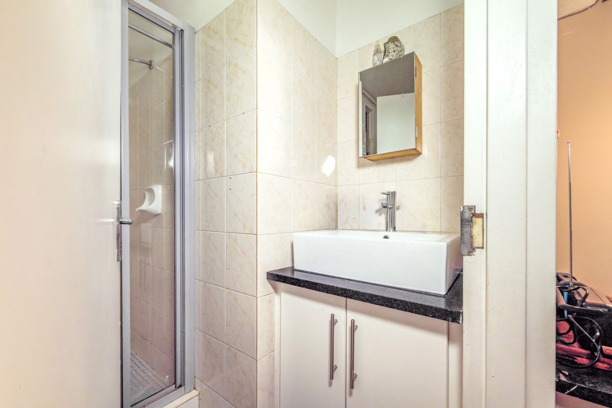 Compact bathroom featuring a shower enclosure, vanity cabinet with a vessel sink, and wall-mounted mirror cabinet with tiled wall finishes.