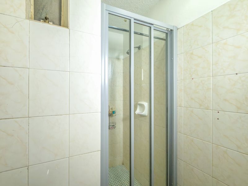 A functional shower stall featuring a sliding glass door and tiled walls, currently requiring some maintenance and cosmetic updates.