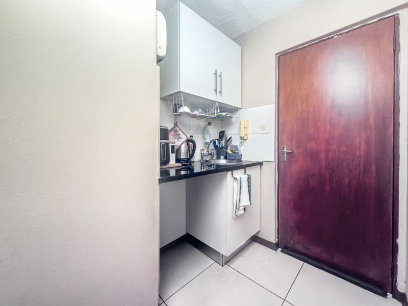 A compact scullery area featuring built-in white cabinetry, a granite countertop with an integrated sink, and tiled flooring.