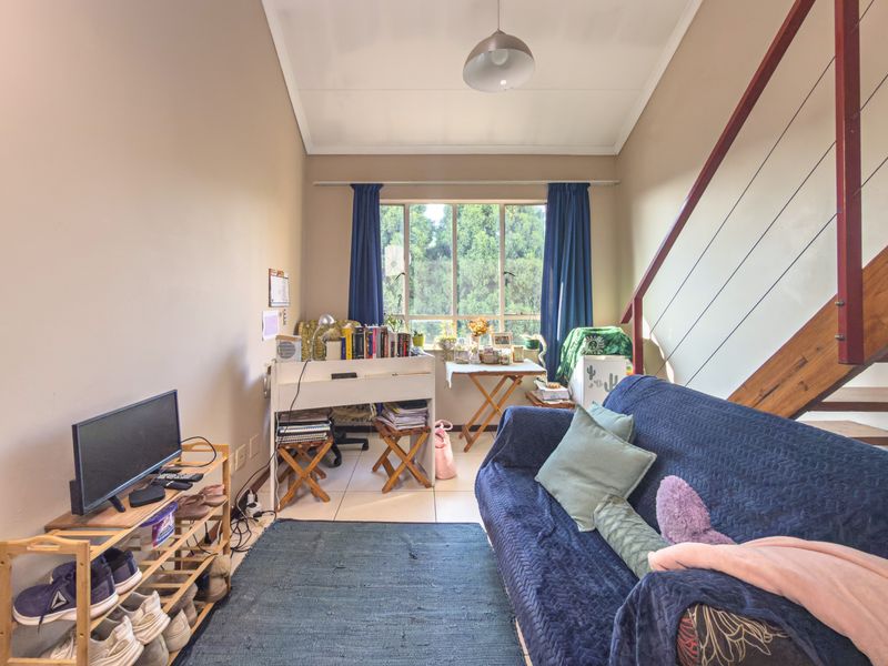 A living area featuring tiled flooring and an internal staircase with a metal railing, providing a functional space with natural light.