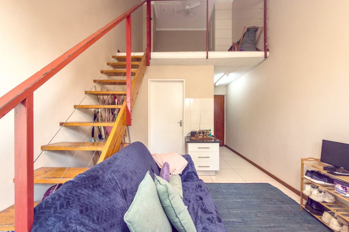 Open-plan living area featuring a mezzanine level, wooden staircase with metal railing, and tiled flooring, offering a versatile layout for modern apartment living.
