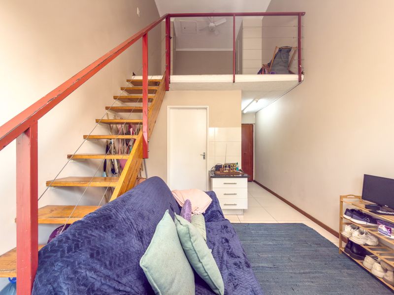 Open-plan living area featuring a mezzanine level, wooden staircase with metal railing, and tiled flooring, offering a versatile layout for modern apartment living.