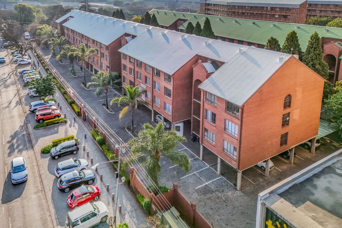 Aerial view of a multi-story brick apartment complex featuring a metal roof, paved parking areas, and established landscaping within a secure perimeter.