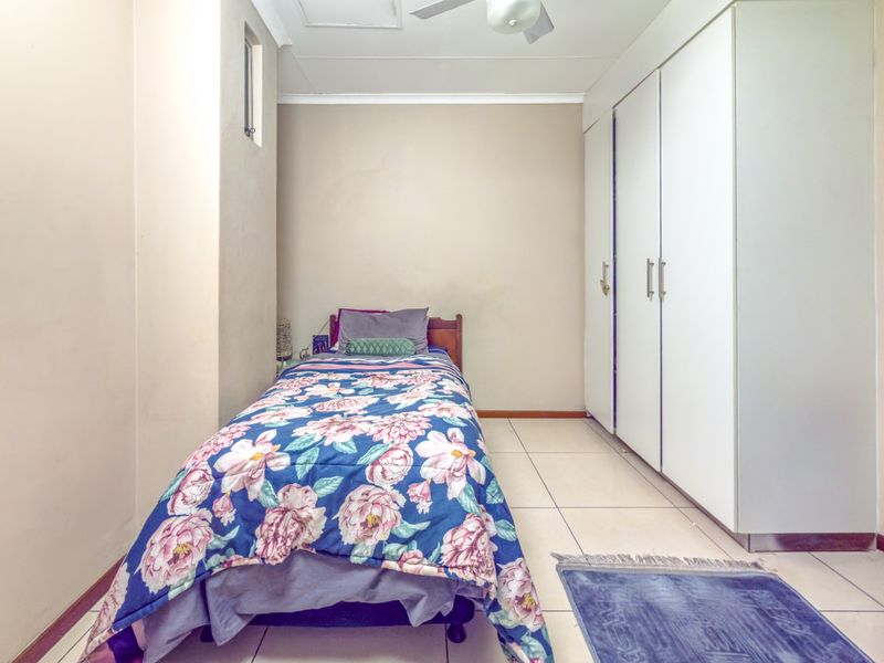 A functional bedroom featuring tiled flooring, a ceiling fan, and ample built-in cupboard storage space.