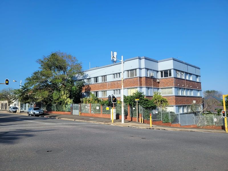 Street-level view of a multi-story brick and painted apartment building featuring secure perimeter fencing and a prominent corner location.