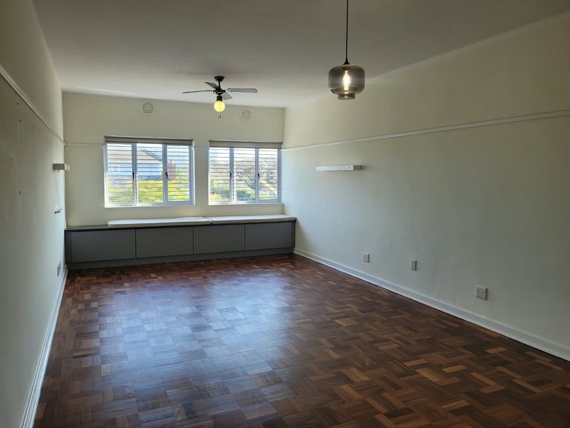 Spacious living area featuring classic parquet flooring, built-in window cabinetry, ceiling fan, and large louvered windows providing ample natural light.