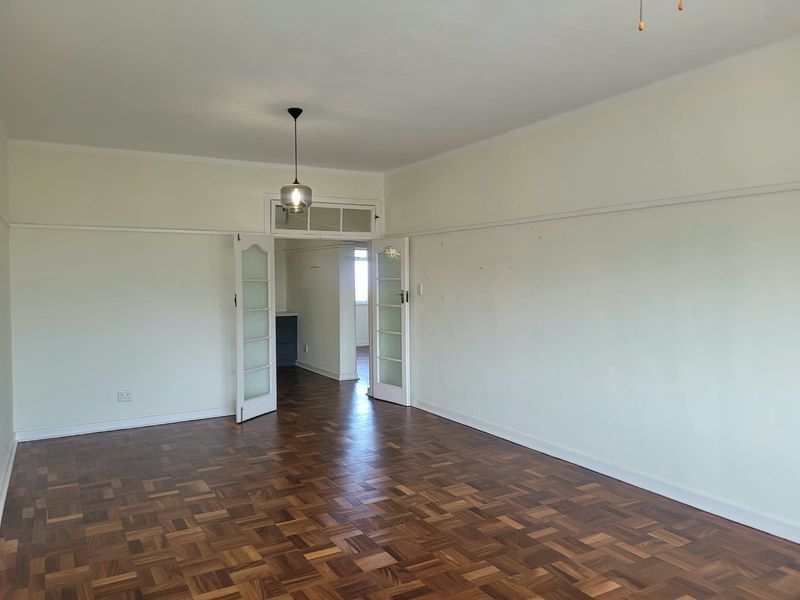 Spacious living area featuring classic parquet flooring, high ceilings with picture rails, and elegant double glass-panelled doors leading to an adjoining room.