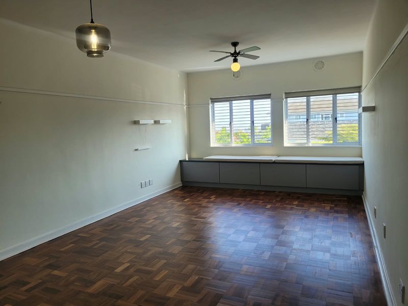 Spacious living room featuring polished parquet flooring, built-in storage cabinetry, ceiling fan, and large windows with blinds.