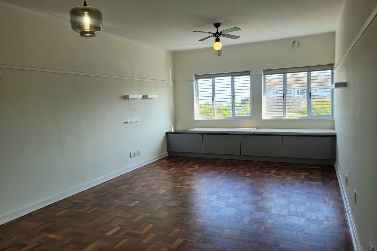 Spacious living room featuring polished parquet flooring, built-in storage cabinetry, ceiling fan, and large windows with blinds.