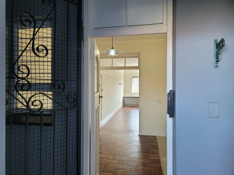View through the entrance door into a vacant hallway featuring classic parquet flooring and a transom window above the internal doorway.