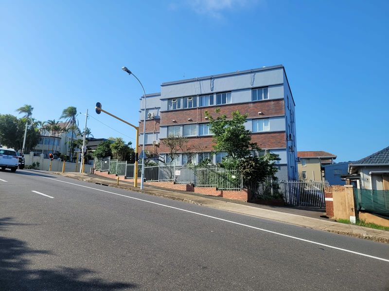 Street-level view of a multi-story apartment building featuring a brick and painted facade with secure perimeter fencing.