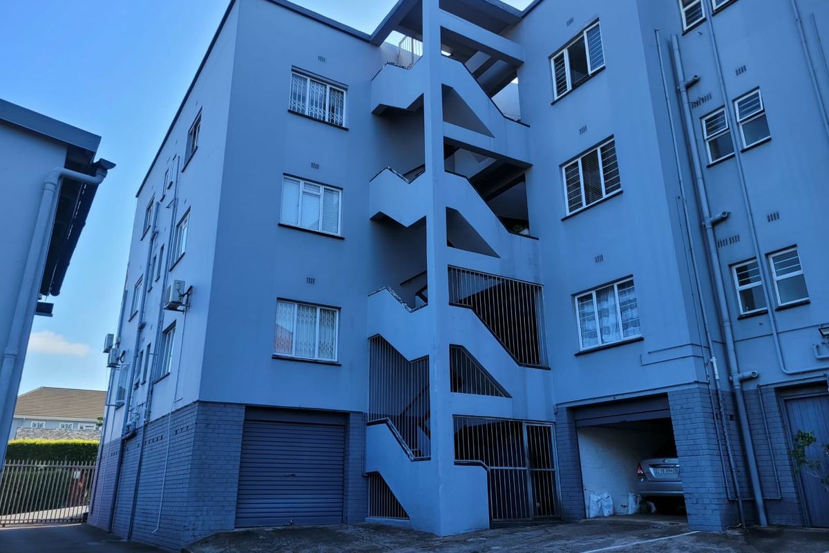 Rear elevation of a multi-story apartment building featuring an external concrete stairwell, security gates, and ground-level parking access.