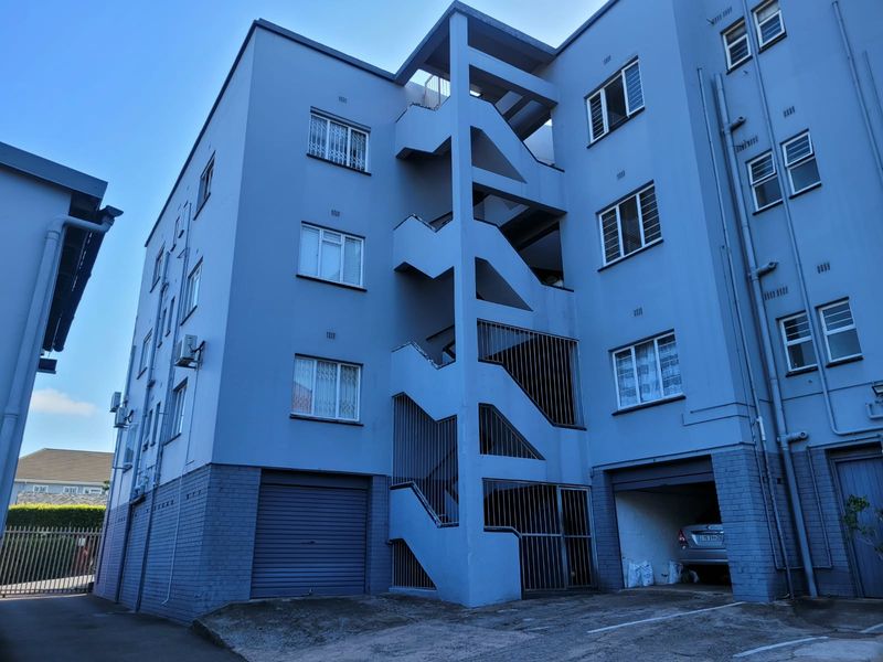 Rear elevation of a multi-story apartment building featuring an external concrete stairwell, security gates, and ground-level parking access.