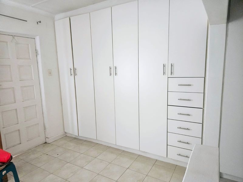 A bedroom featuring extensive white built-in cupboards with integrated drawers and tiled flooring.