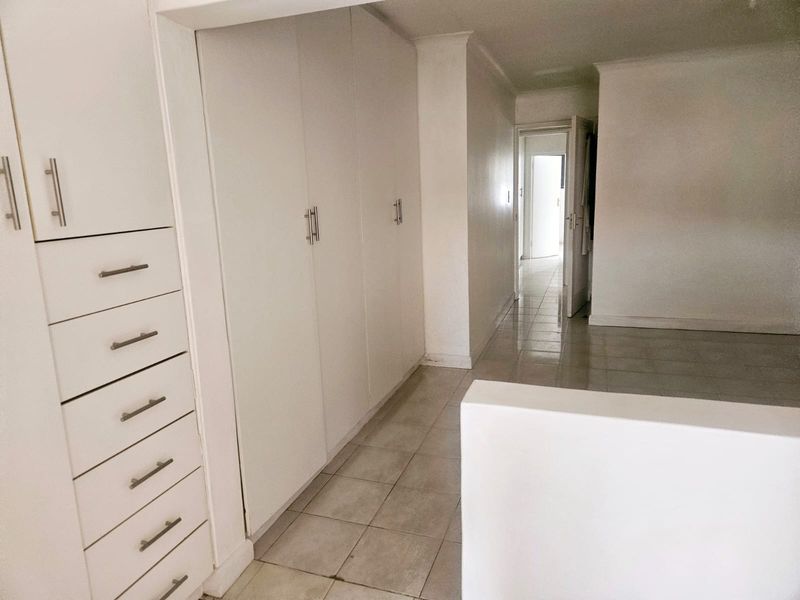A bright, empty hallway featuring extensive built-in storage cupboards and neutral tiled flooring, leading towards an adjacent room.