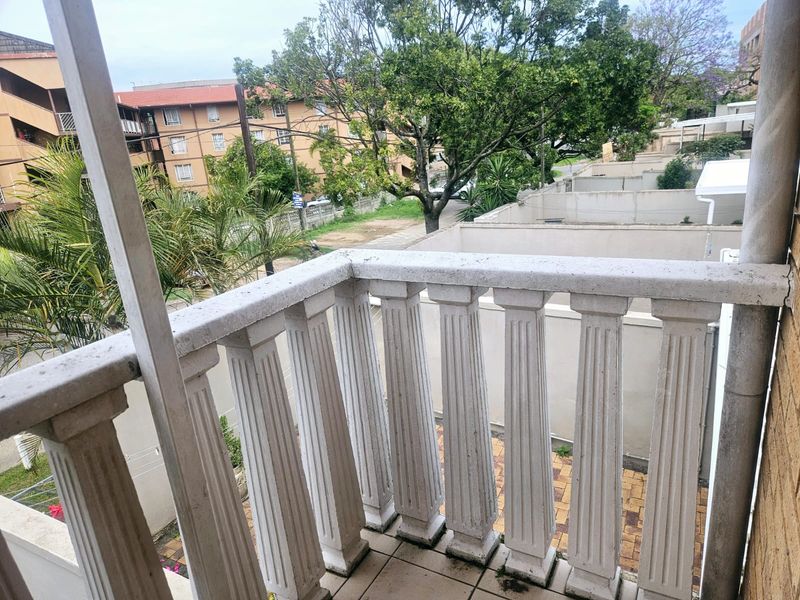 A balcony featuring a classic concrete balustrade and tiled flooring, overlooking the surrounding residential complex and neighborhood.