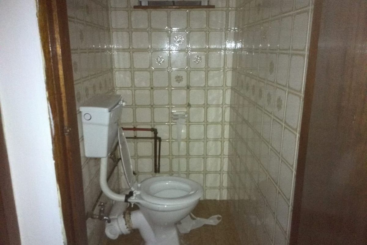 A small, dated bathroom featuring a standard toilet, tiled walls, and exposed plumbing, requiring modernization and cosmetic updates.