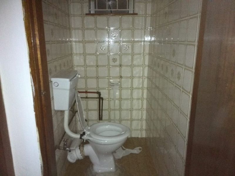 A small, dated bathroom featuring a standard toilet, tiled walls, and exposed plumbing, requiring modernization and cosmetic updates.