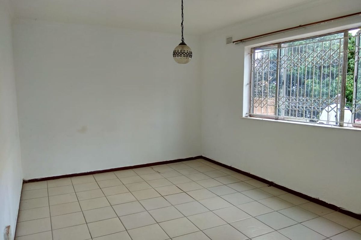 An empty living room featuring tiled flooring, a pendant light fixture, and a window fitted with security bars.