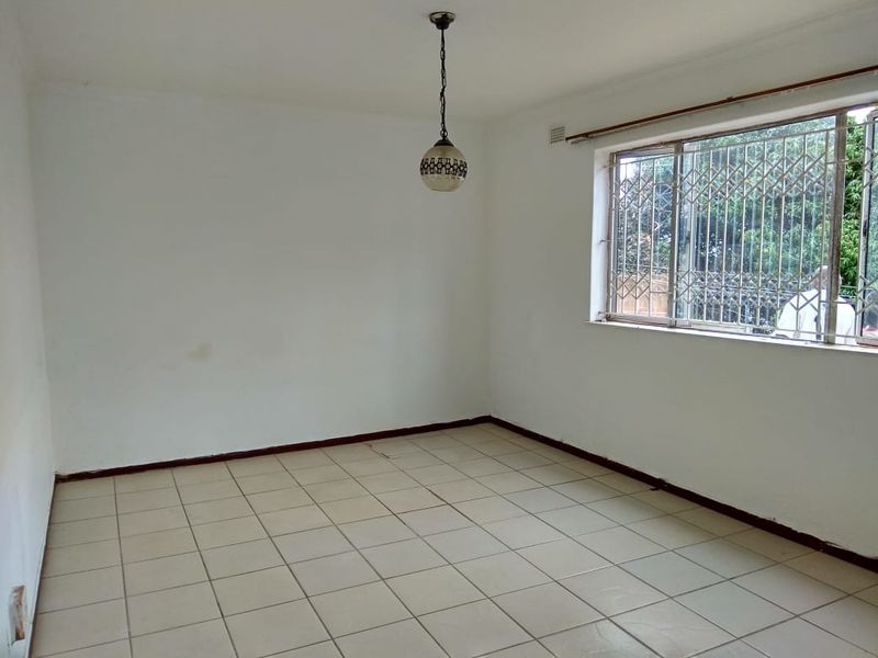 An empty living room featuring tiled flooring, a pendant light fixture, and a window fitted with security bars.