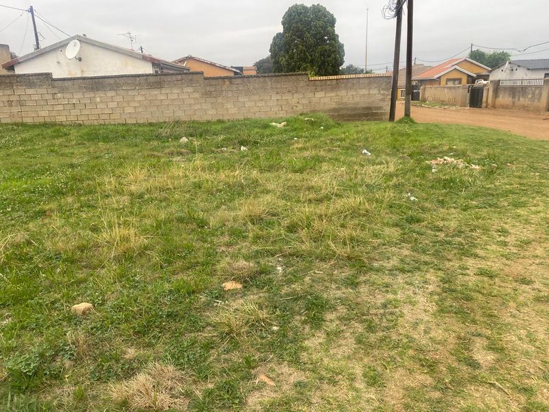 A vacant residential plot featuring a perimeter boundary wall and direct street access, suitable for future development.