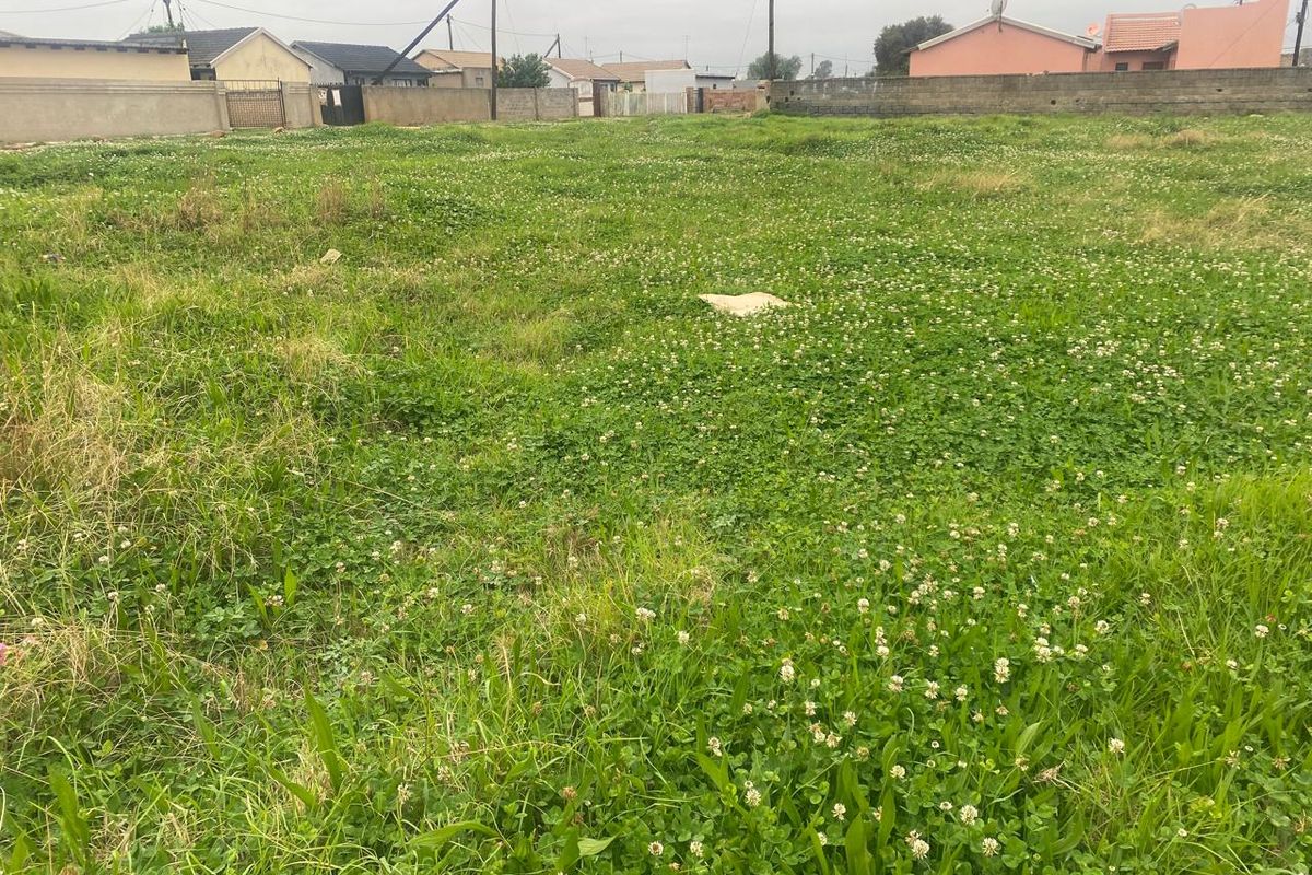 A vacant residential plot of land featuring established grass cover and enclosed by perimeter boundary walls in a suburban neighborhood setting.