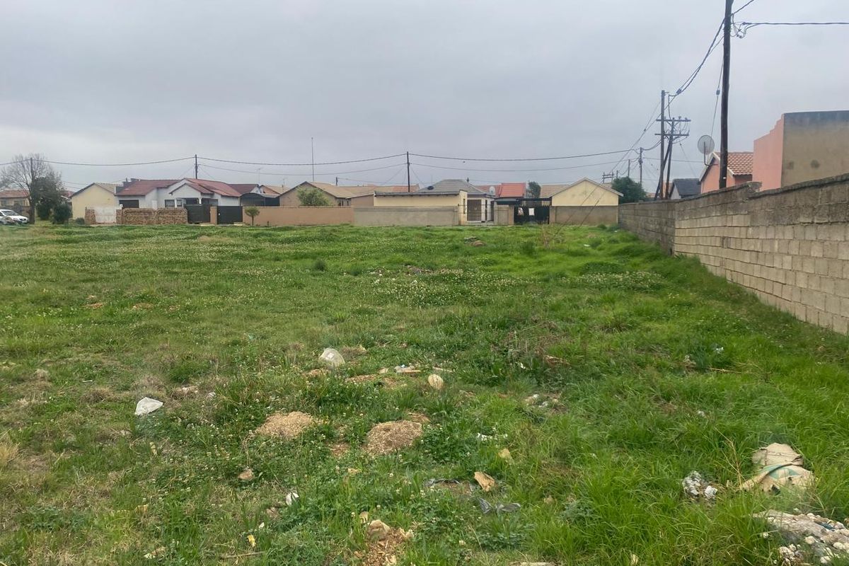 A vacant residential plot featuring a boundary wall and access to utility services, ready for development in a established neighborhood.
