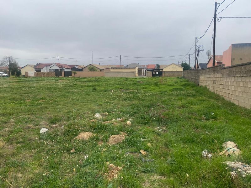 A vacant residential plot featuring a boundary wall and access to utility services, ready for development in a established neighborhood.