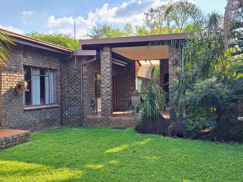 Rear view of a face brick house featuring a covered patio area, established garden, and sliding door access to the interior living space.