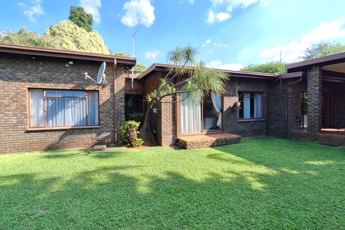 Rear view of a face brick house featuring a well-maintained lawn, sliding glass doors, and a covered patio area.