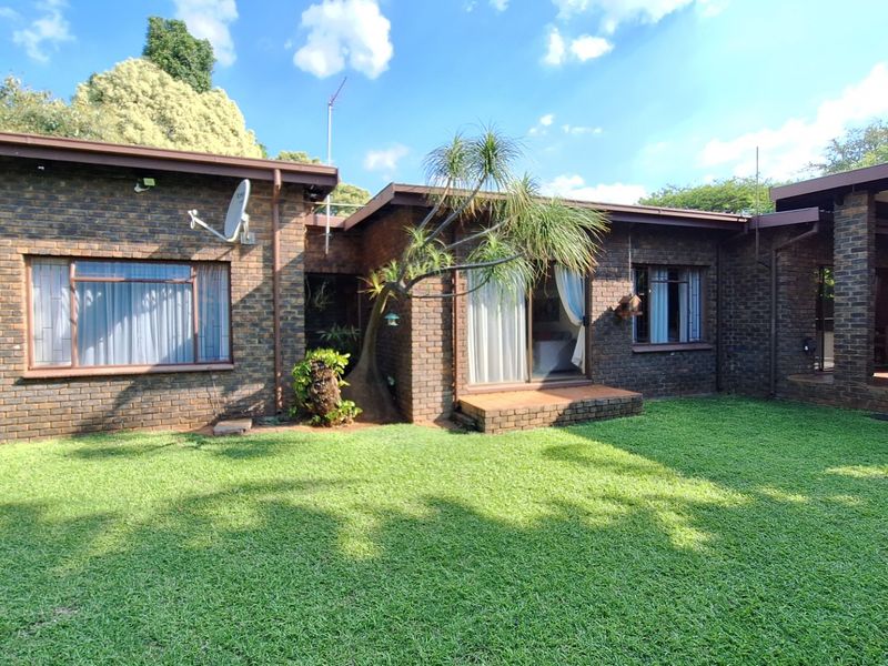 Rear view of a face brick house featuring a well-maintained lawn, sliding glass doors, and a covered patio area.