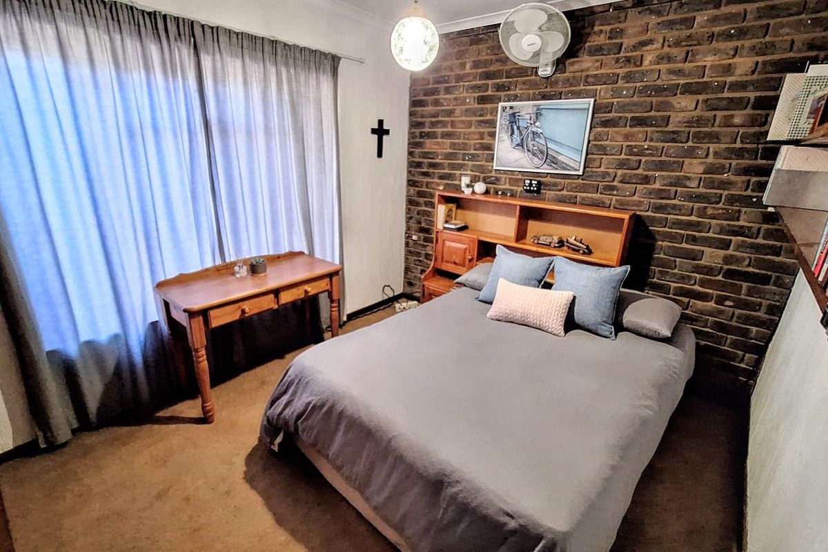 A bedroom featuring an exposed brick feature wall, neutral carpeting, and a ceiling fan, offering a cozy and textured living space.