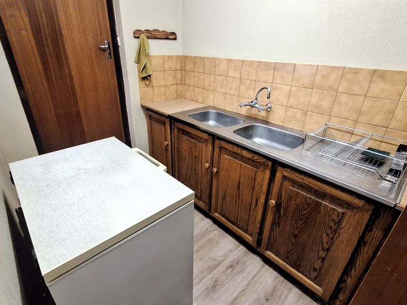 A functional scullery area featuring wooden cabinetry, a double stainless steel sink, and tiled splashbacks, providing practical utility space.