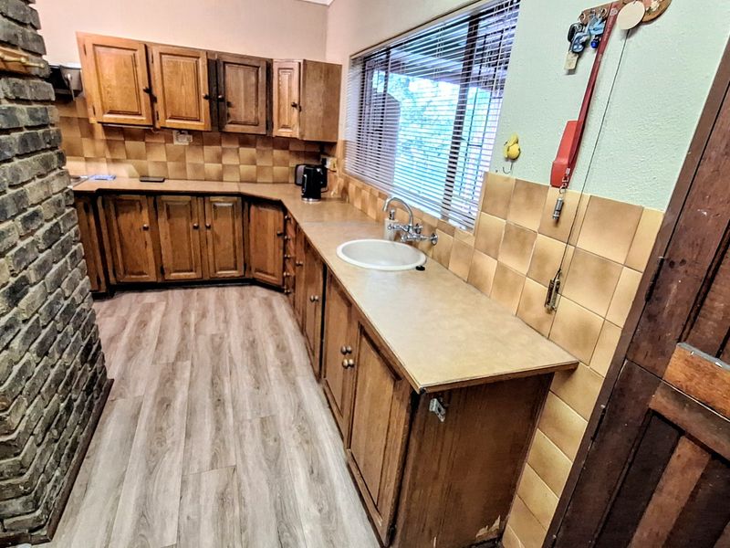 A dated kitchen featuring wooden cabinetry, laminate countertops, a tiled backsplash, and a prominent brick feature wall.