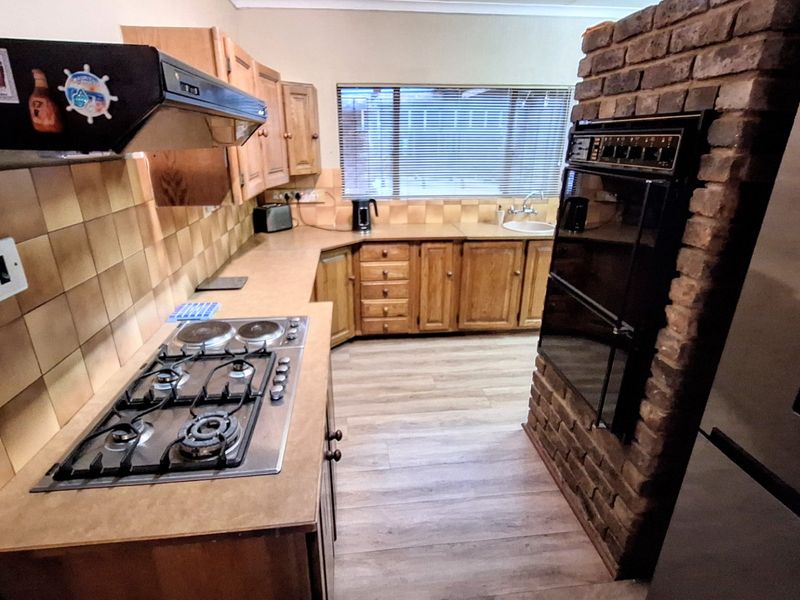 A functional kitchen featuring wooden cabinetry, a gas hob with extractor, built-in double oven, and a distinctive brick feature wall.