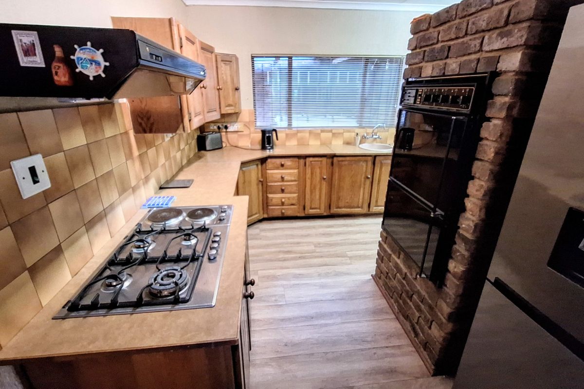 A functional kitchen featuring wooden cabinetry, a gas hob with extractor, built-in double oven, and a distinctive brick feature wall.