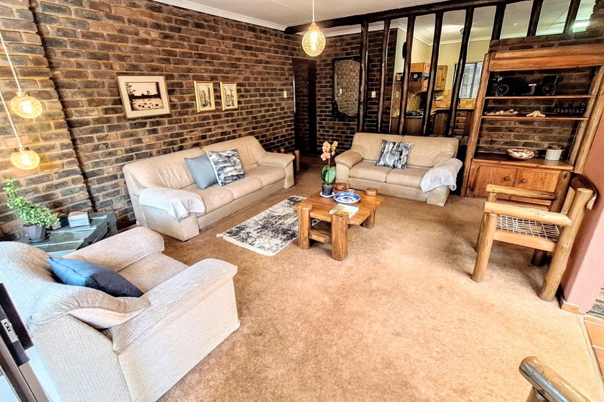 A living room featuring an exposed brick feature wall, timber room divider, and neutral carpeting, offering a rustic aesthetic with potential for modern updates.