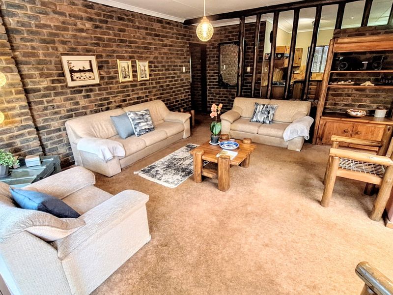 A living room featuring an exposed brick feature wall, timber room divider, and neutral carpeting, offering a rustic aesthetic with potential for modern updates.