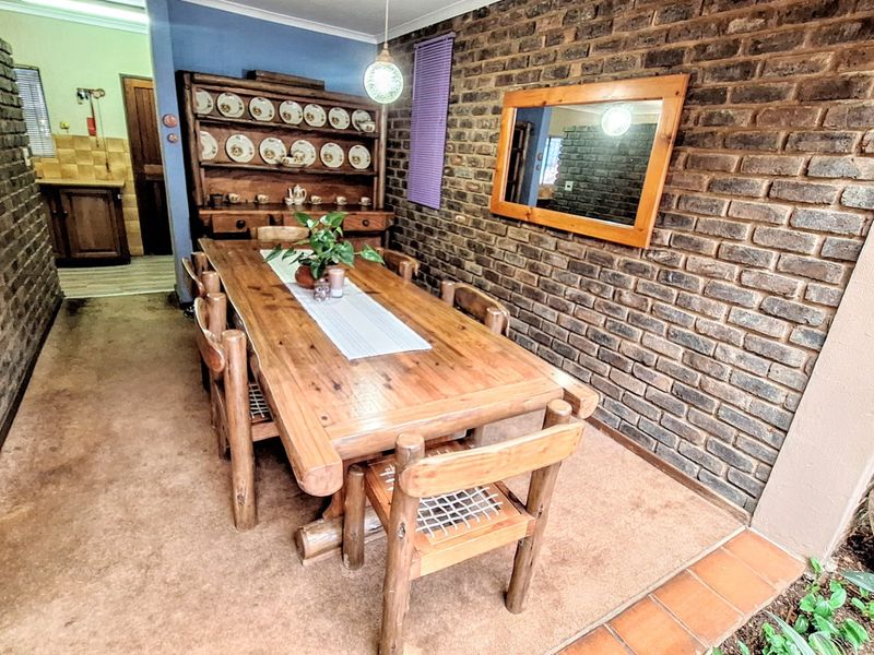 A rustic dining room featuring exposed brick walls, tiled flooring, and a view into the adjacent kitchen area.
