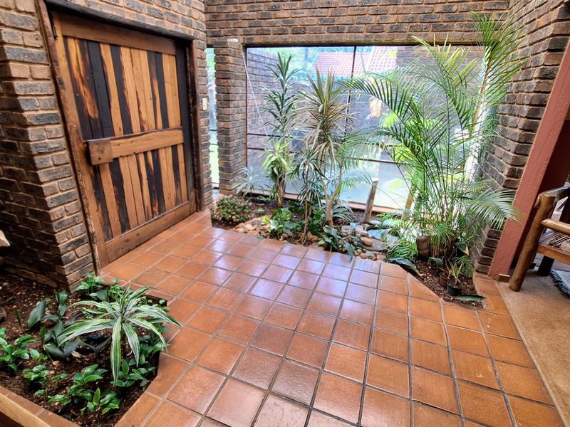 An enclosed patio area featuring exposed brick walls, terracotta floor tiling, and an integrated internal garden bed with a rustic timber door.