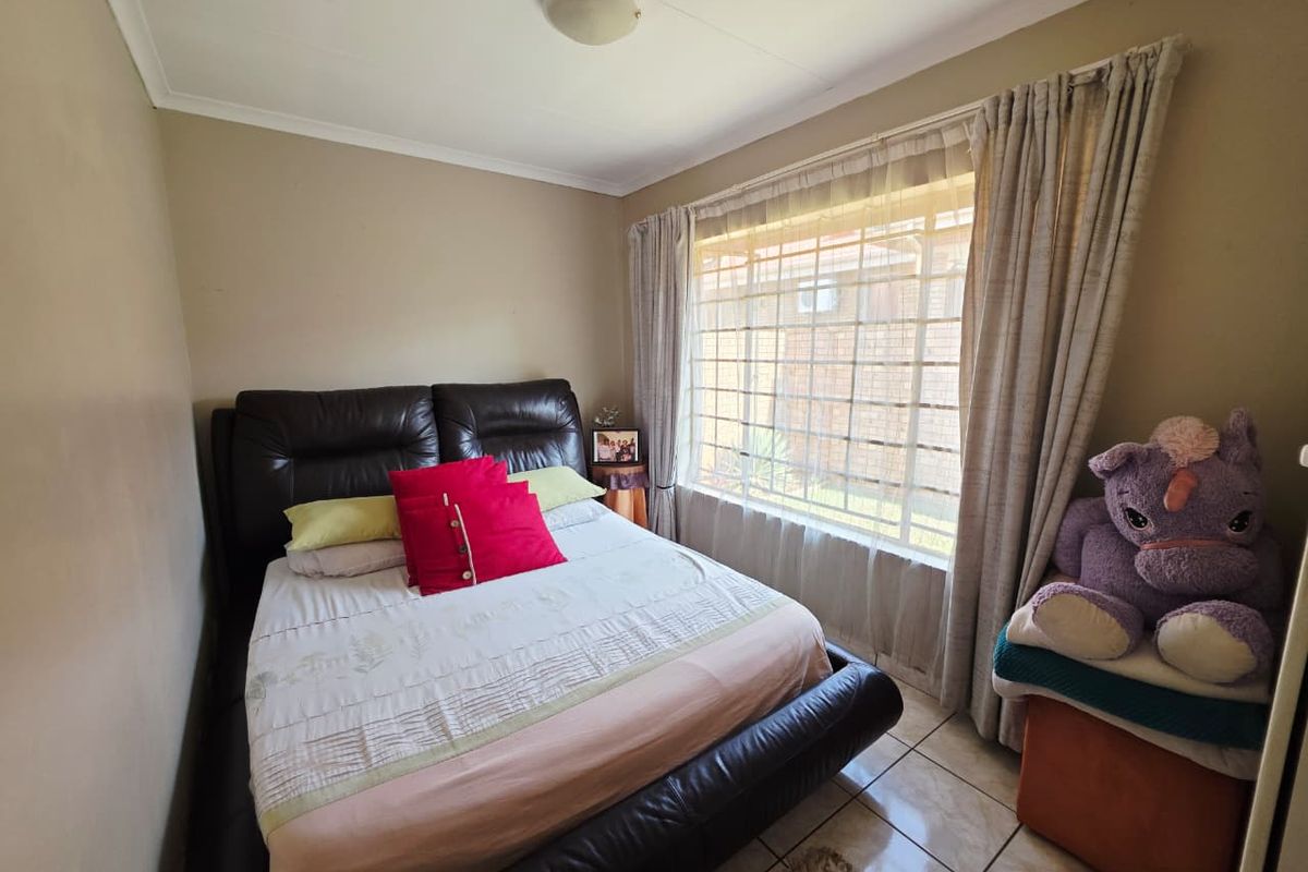 A standard bedroom featuring tiled flooring, a large window with security bars, and neutral wall finishes.
