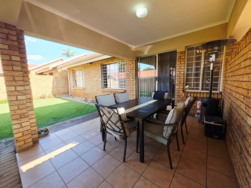 A covered patio area featuring tiled flooring, brick pillars, and direct access to the garden through sliding glass doors.