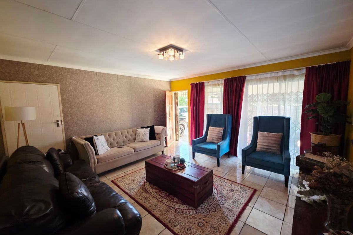 A spacious living room featuring tiled flooring, textured accent wallpaper, and a sliding glass door providing natural light and access to the exterior.