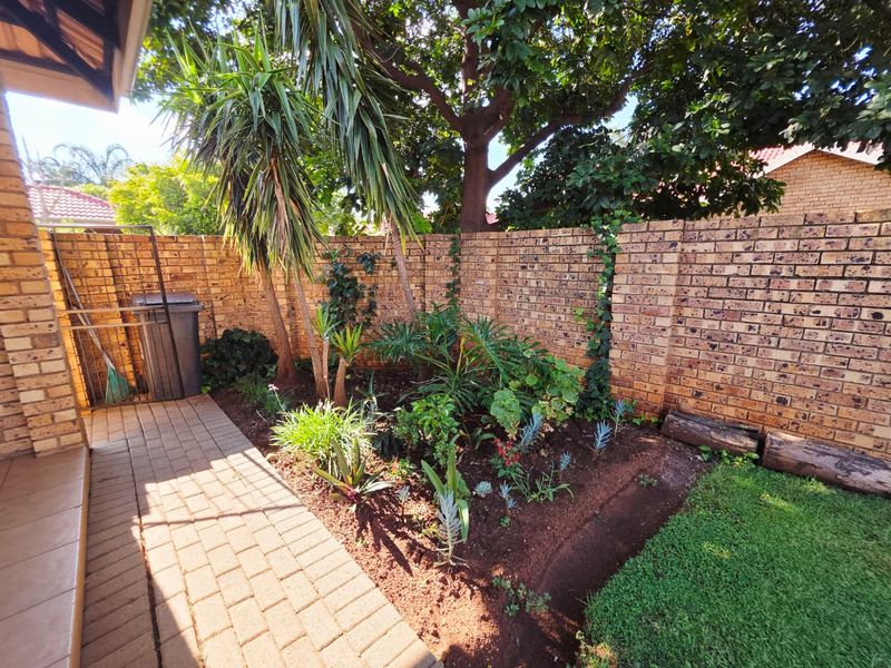 A private rear garden area featuring a paved walkway, established garden beds, and a secure brick boundary wall.