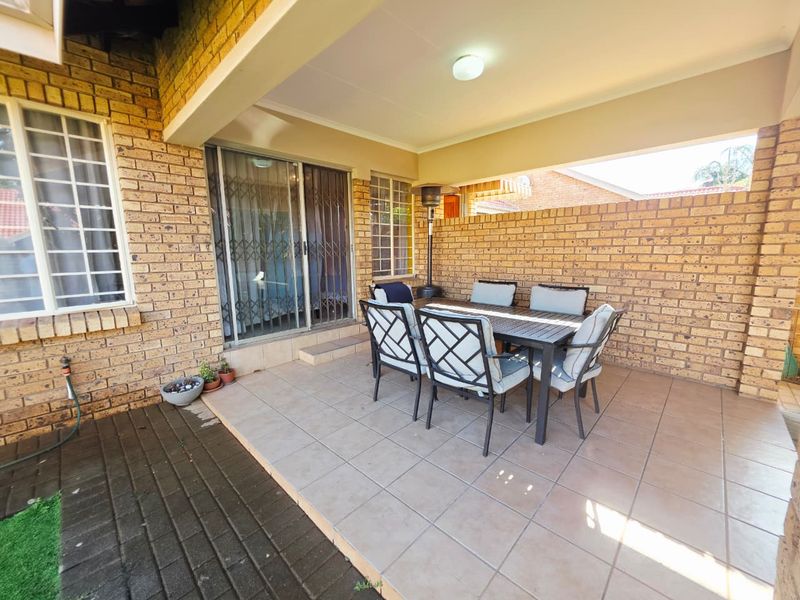 A covered outdoor patio featuring tiled flooring and exposed brick walls, providing a functional space for outdoor dining and relaxation.