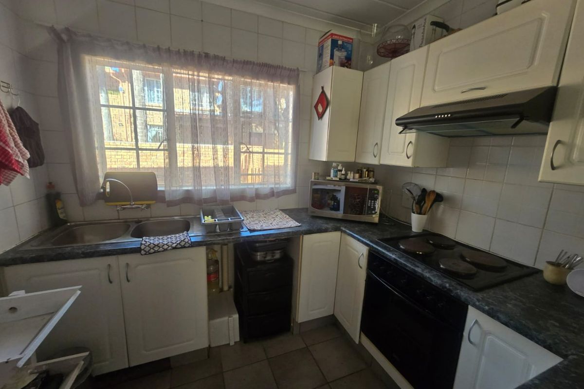 A functional kitchen featuring white cabinetry, dark laminate countertops, a built-in oven with electric hob, and a double bowl sink under a window.