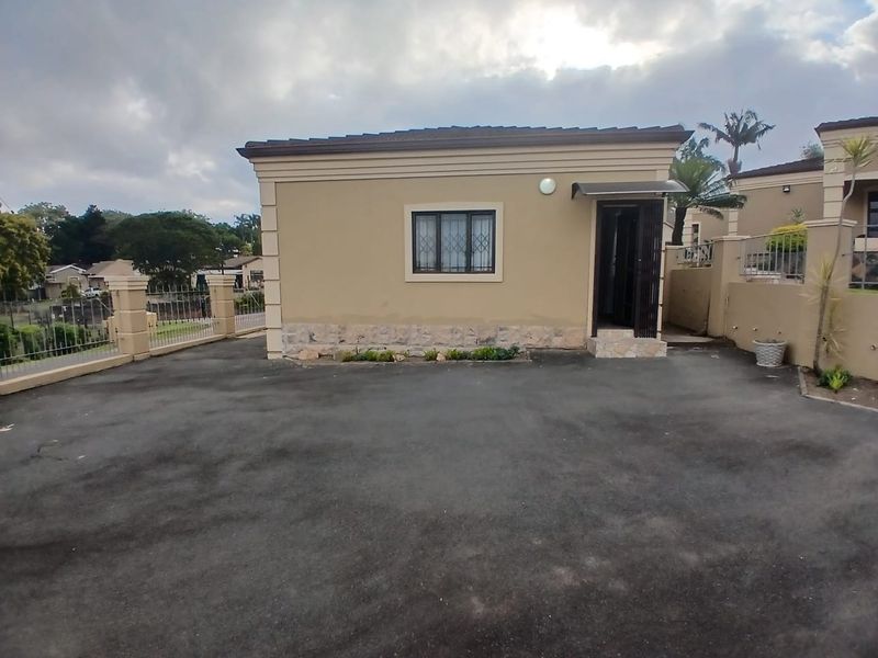 Front exterior view of the cottage featuring an asphalt driveway, stone cladding accents, and secure entrance with security gate and window bars.