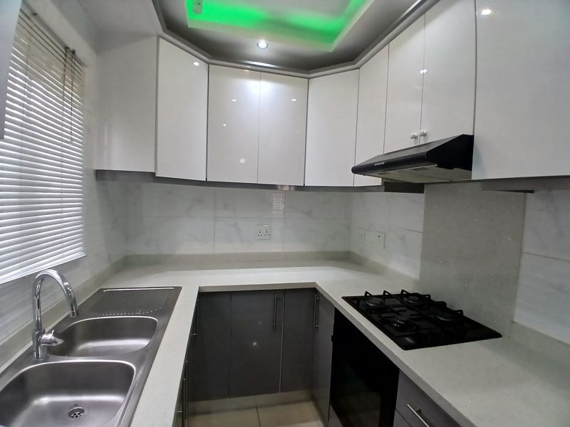 Modern kitchen featuring high-gloss cabinetry, stone countertops, integrated gas hob, oven, extractor fan, and a double bowl stainless steel sink.
