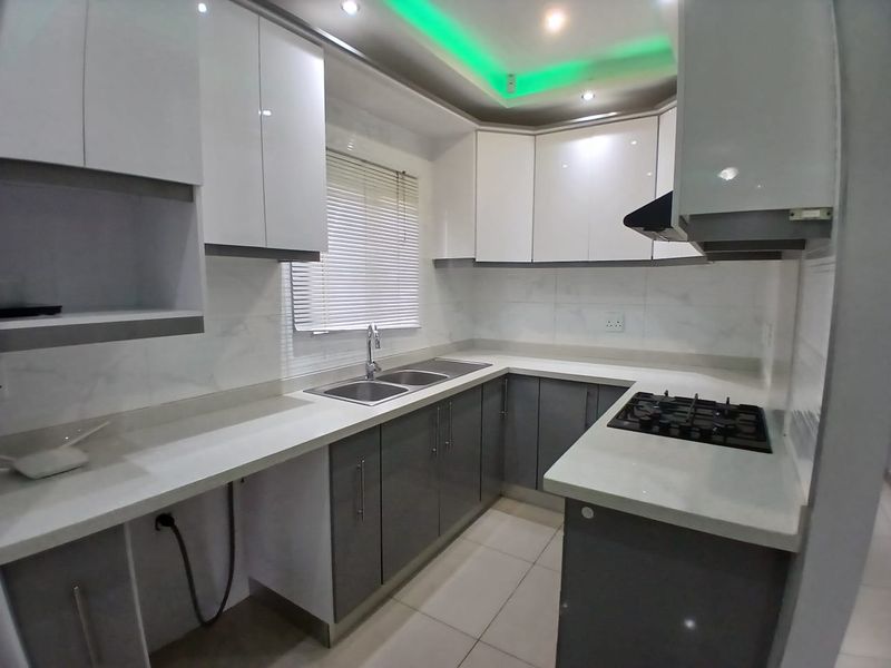 Modern kitchen featuring sleek two-tone cabinetry, stone countertops, integrated gas hob, extractor fan, and recessed ceiling lighting with ambient feature lighting.
